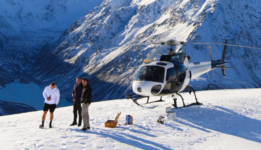 Helicopter parked on a mountain overlooking glaciers while Richie McCaw and passengers enjoy picnic